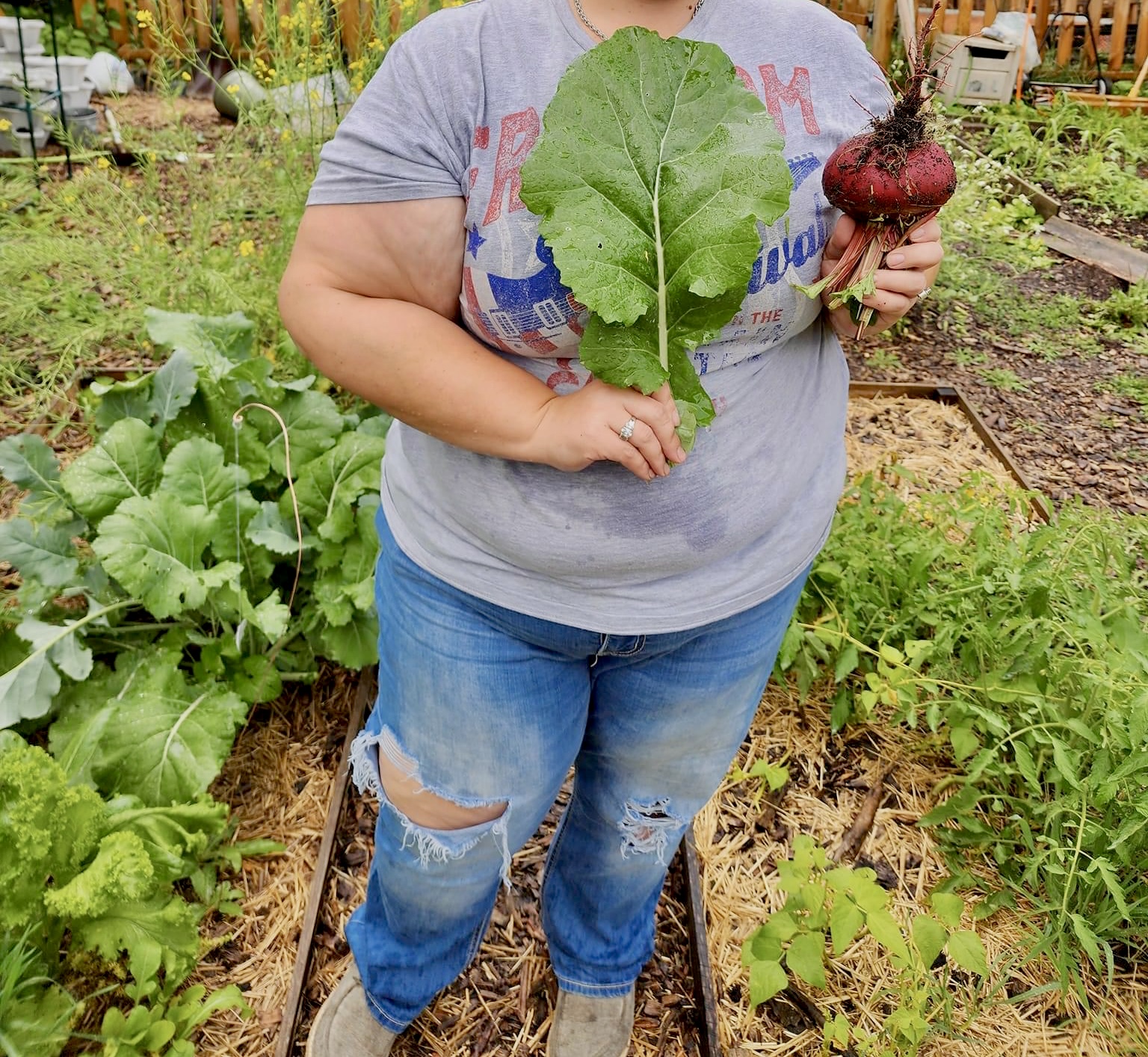 Heather holds a large Detroit Red Beet and a large leaf Kale while standing in her garden
